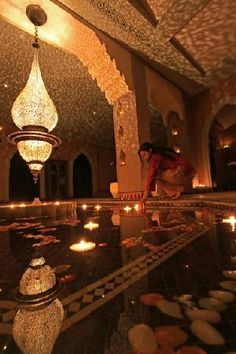 a woman kneeling down in front of a pool filled with water surrounded by lit candles