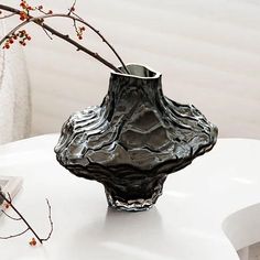 a black vase sitting on top of a white table next to a branch with flowers