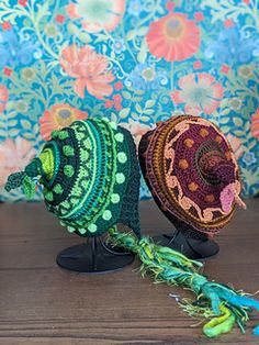 two crocheted hats sitting on top of a wooden table next to a colorful wall