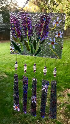 a wind chime with purple flowers hanging from it's side in the grass