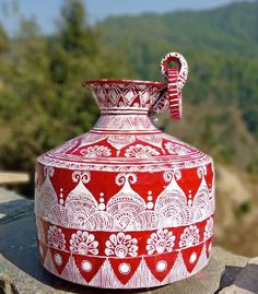 a red and white vase sitting on top of a rock