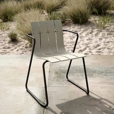 a white chair sitting on top of a cement floor next to tall grass and bushes