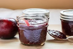 two jars filled with jam sitting on top of a wooden table next to an apple