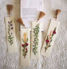 three embroidered bookmarks with flowers and leaves on them sitting on a white tablecloth