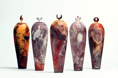 five vases are lined up in a row on a white surface, one is orange and the other is brown