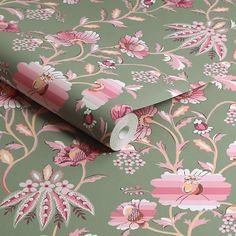 a green and pink floral wallpaper with flowers on the side, next to a roll of toilet paper