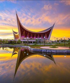 a large building sitting next to a body of water under a colorful sky at sunset