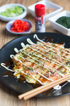 a black plate topped with food and chopsticks on top of a wooden table