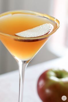 a close up of a drink in a glass near an apple