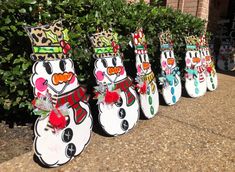 snowmen with hats and scarves are lined up in front of some bushes on the sidewalk