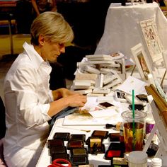 a woman sitting at a table with lots of art supplies