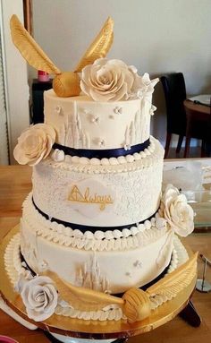 a three tiered wedding cake with white flowers and gold wings on top is sitting on a table