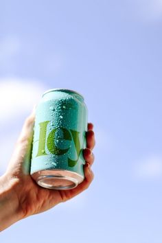 a hand holding a can of soda against a blue sky