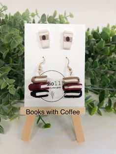 a pair of books with coffee earrings sitting on top of a wooden stand next to green leaves