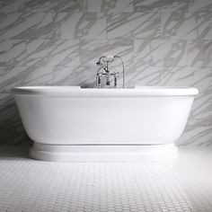 a white bath tub sitting on top of a tiled floor next to a wall mounted faucet