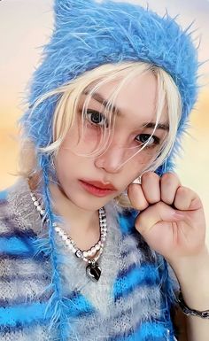 a young woman wearing a blue furry hat and sweater posing for the camera with her hand on her face