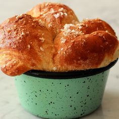 two croissants sitting in a green cup on a marble counter top with white speckles