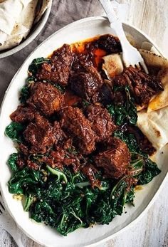 a white plate topped with meat and spinach next to pita bread on top of a table