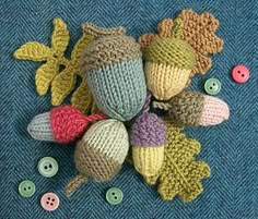 several knitted acorns and leaves laying on a blue surface with buttons around them