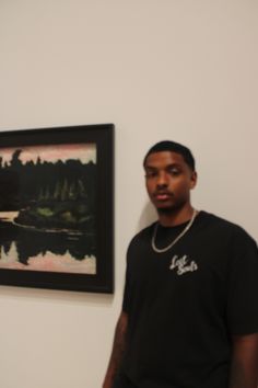 a man standing in front of a painting on the wall next to a framed photo