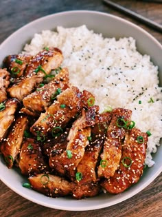 a white bowl filled with chicken and rice on top of a wooden table next to chopsticks