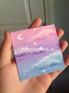 a hand holding up a piece of paper with the sky and stars painted on it