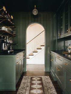 a kitchen with green cabinets and an area rug in front of the door that leads to another room