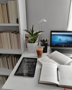 an open book is sitting on a desk next to a laptop and bookshelf