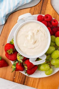 a plate with grapes and strawberries next to a bowl of yogurt on a cutting board