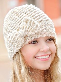 a woman with blonde hair wearing a white knitted hat and smiling at the camera