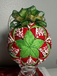 a christmas ornament is sitting on top of a glass vase with a green bow