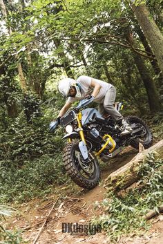 a man riding on the back of a dirt bike down a forest trail in front of trees