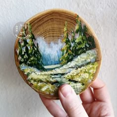 a hand holding a small wooden bowl with a painting on it