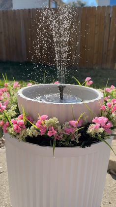 a water fountain surrounded by pink flowers in a white planter with sprinkles on top