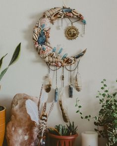 there is a wall decoration with feathers and beads hanging on the wall next to potted plants