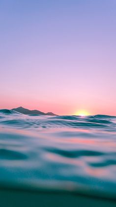 the sun is setting over the ocean as seen from the water's surface, with mountains in the distance