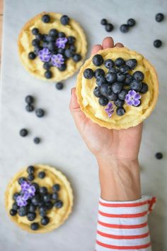 a person holding up a pastry with blueberries on it and flowers in the middle