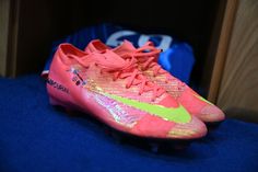 a pair of pink and yellow soccer cleats sitting on top of a blue surface