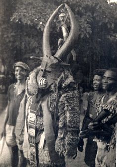 an old black and white photo of people walking with an animal mask on it's head