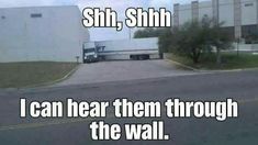 a semi truck driving down a street next to a tall building with the words shr, shih i can hear them through the wall