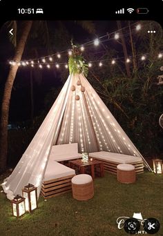 a teepee with lights on it is in the grass near some benches and stools