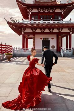 a woman in a red dress walking next to a man in a black suit