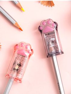 two pencils are laying next to each other on a pink surface with various items