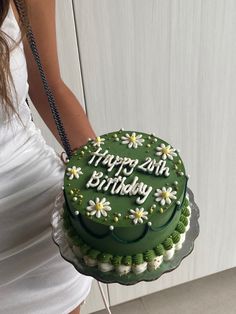 a woman holding a green birthday cake with daisies on it