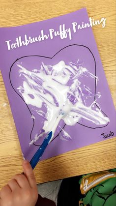 a child's hand is holding a paintbrush and painting on a purple paper