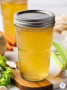 a jar filled with liquid sitting on top of a wooden cutting board next to carrots and celery