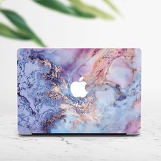 an apple laptop on a marbled surface with a plant in the backgroud