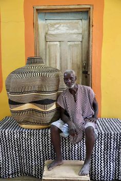 a man sitting next to two large vases on top of a bench in front of a yellow wall