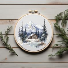 a cross stitch pattern with a cabin in the woods and pine trees on it, surrounded by greenery