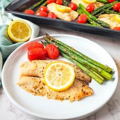 chicken, asparagus and tomatoes on a white plate next to a tray of lemons